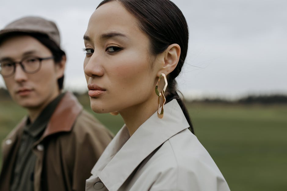 Stylish couple posing outdoors in elegant coats, highlighting fashion and elegance on a cloudy day.