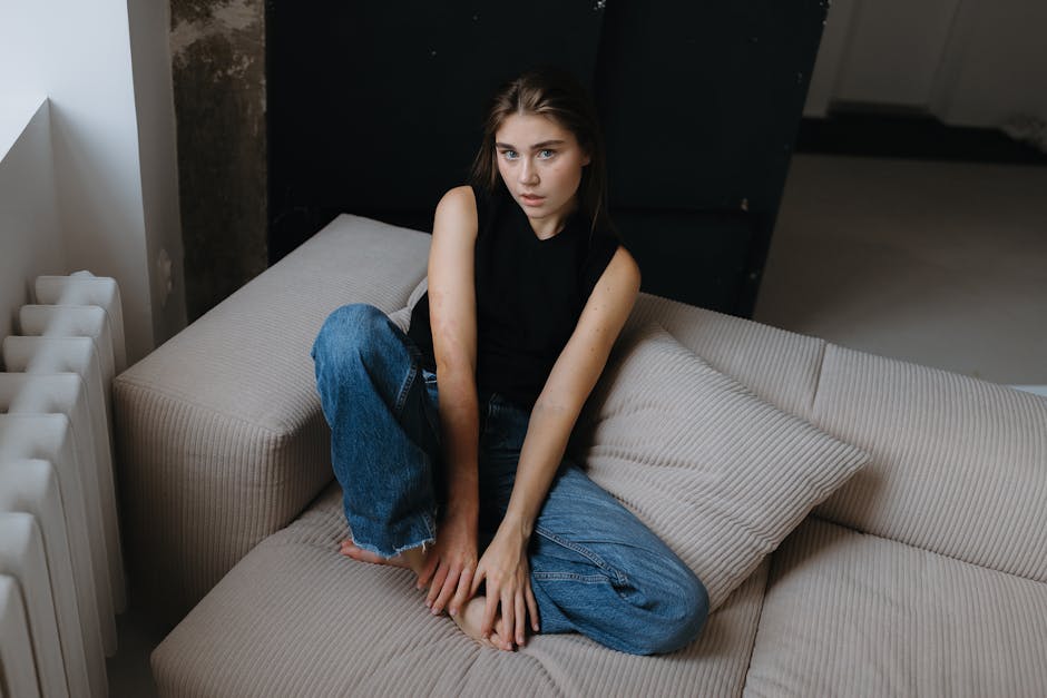 Portrait of a young woman in a black tank top and jeans sitting on a beige sofa.