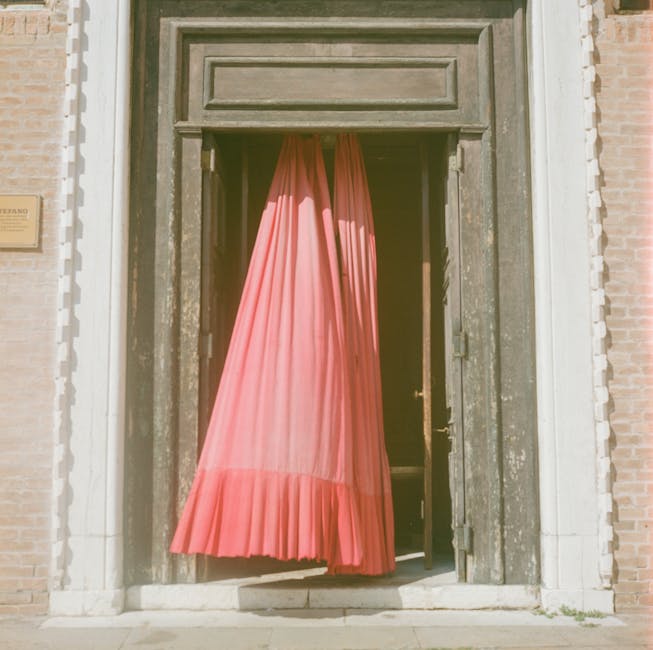 A pink curtain elegantly drapes a wooden door in Venice, Italy, highlighting the city's classic architecture.