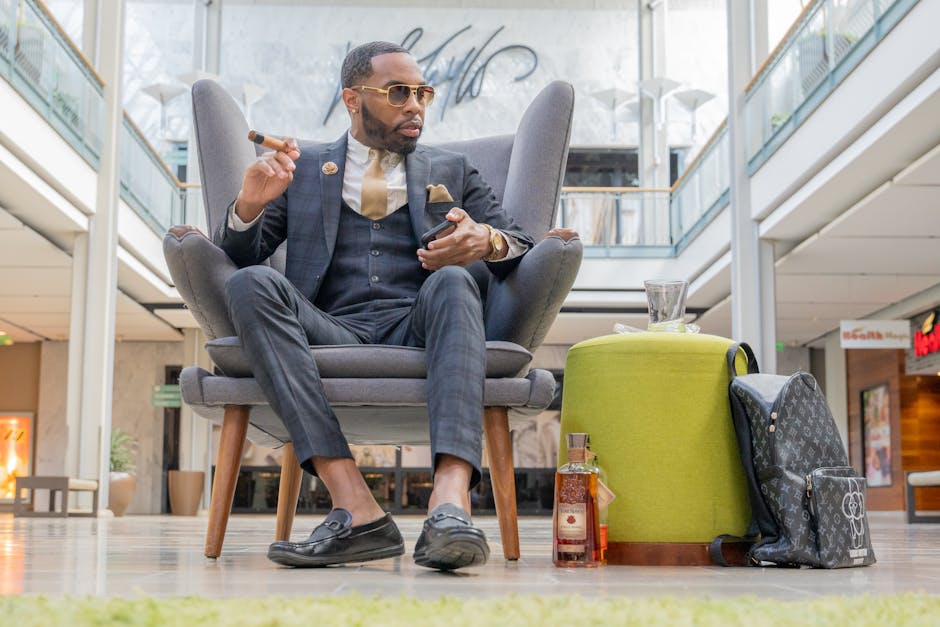 A fashionable man in formal attire enjoying a cigar and whiskey in a luxurious setting.