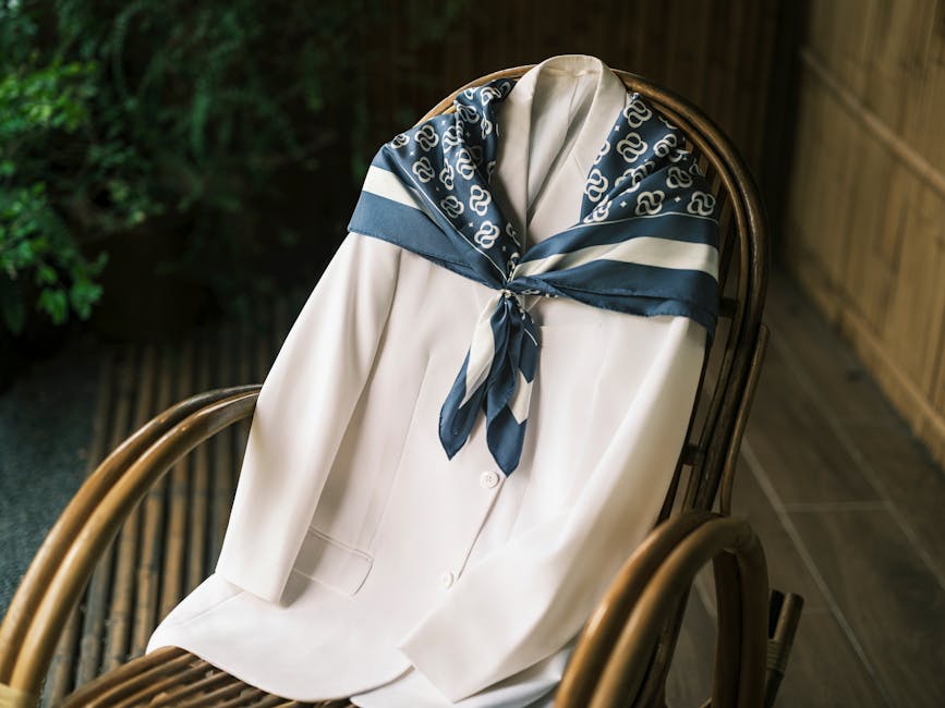 White coat draped with a patterned blue silk scarf on a wooden chair in a stylish setting.