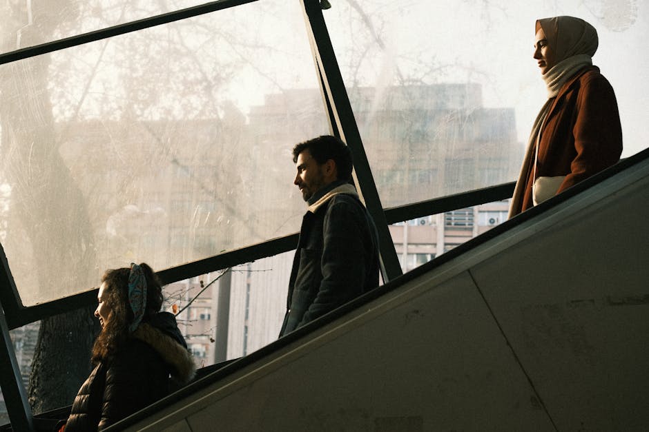Three adults wearing warm clothing use an indoor escalator in a city setting.