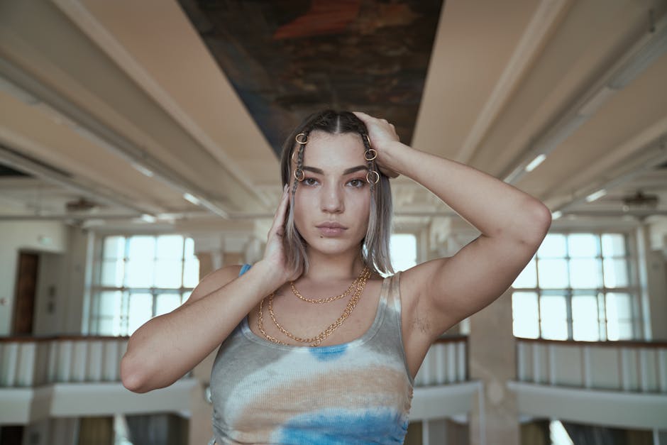 Stylish woman in a tank top poses indoors, showcasing elegant jewelry and modern hairstyle.
