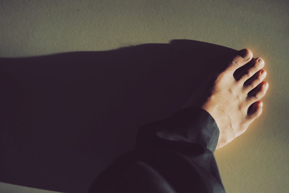 A close-up photo capturing a bare foot casting a dramatic shadow on the ground.
