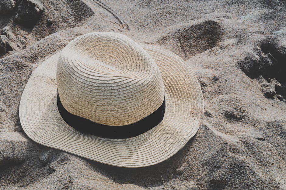 A straw hat with a black band resting on a sandy beach, highlighting summer vibes.