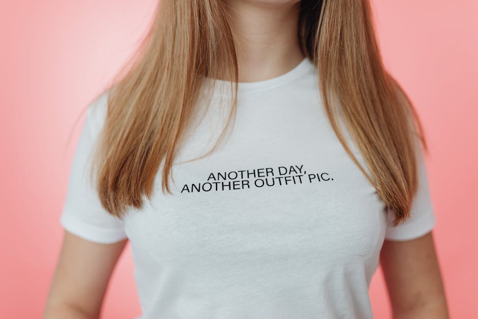 Close-up of a t-shirt with the slogan 'ANOTHER DAY, ANOTHER OUTFIT PIC' against a pink background.